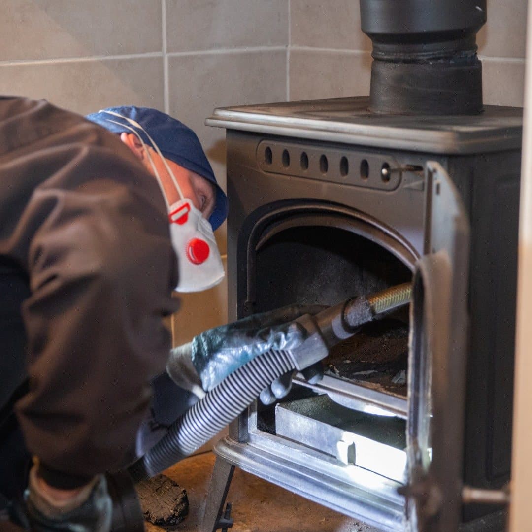 Rob Whitfield in a dust mask vacuuming the inside of a stove during a sweep