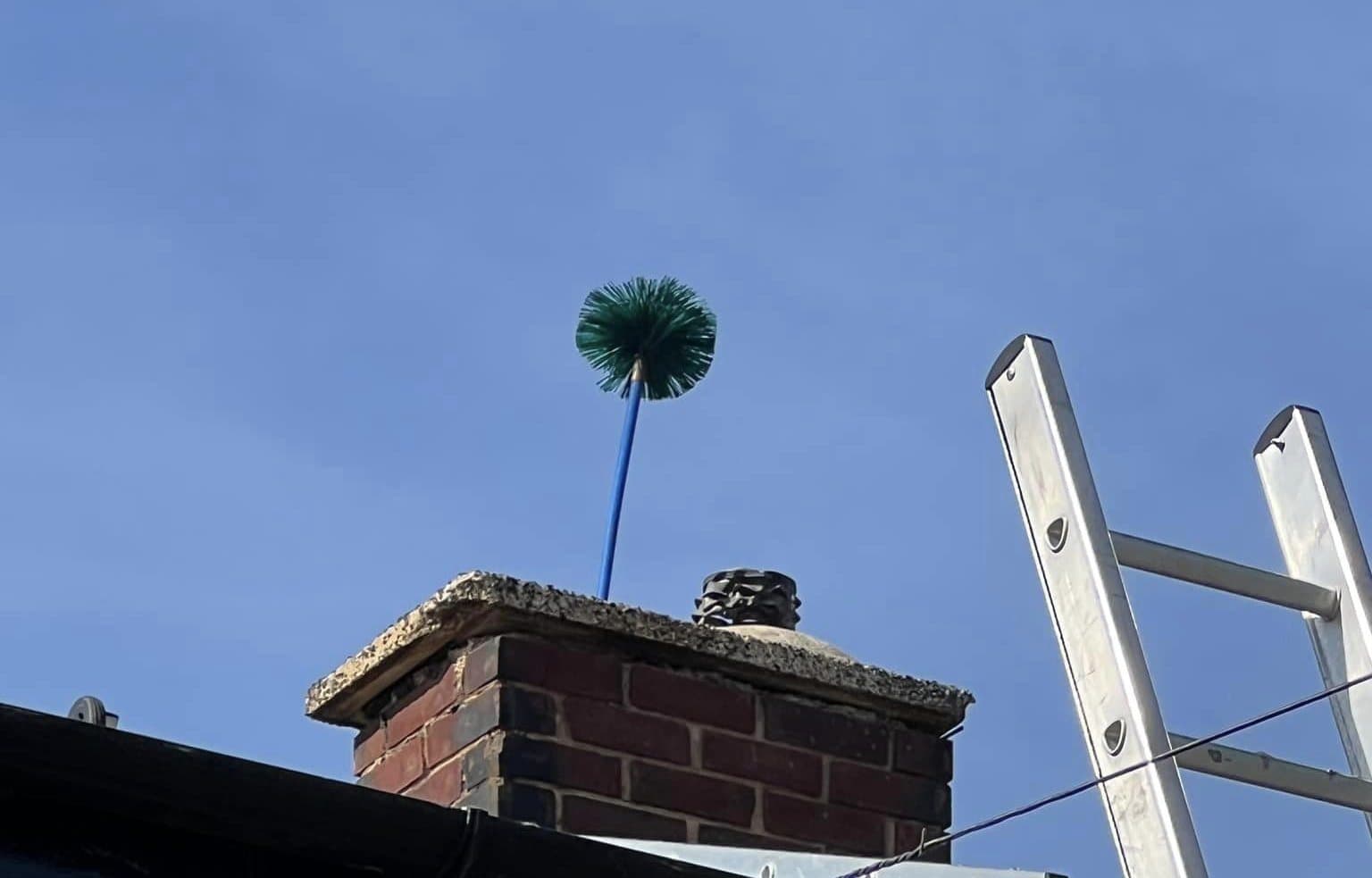 Chimney brush emerging from a chimney pot against a blue sky during a power sweep