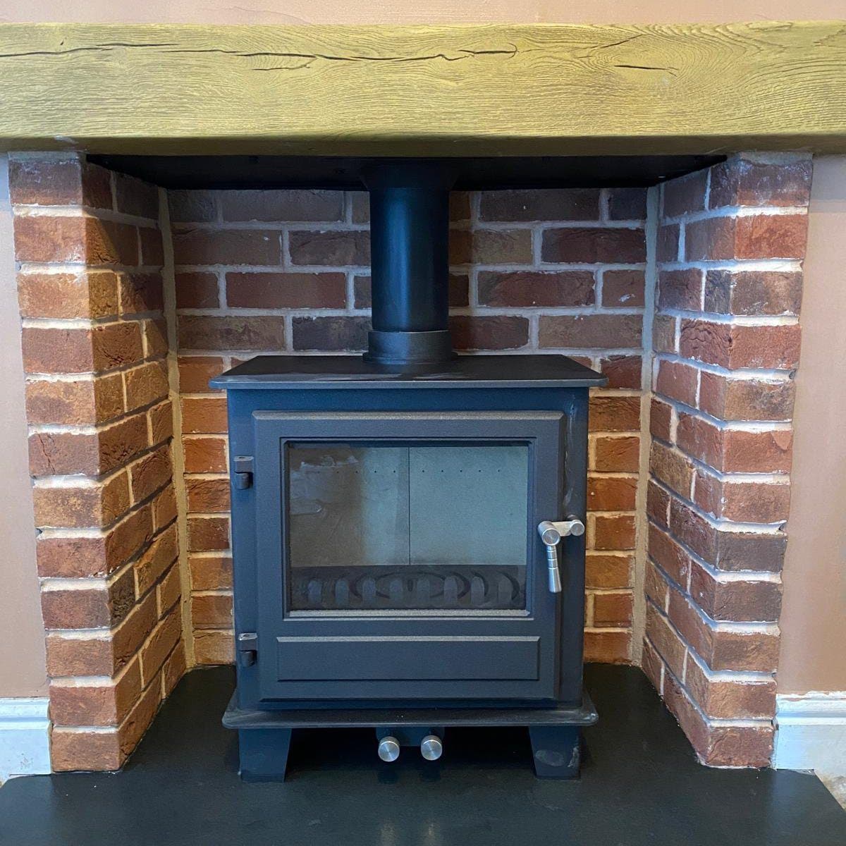 Finished wood burning stove installed in an exposed brick chamber with an oak beam