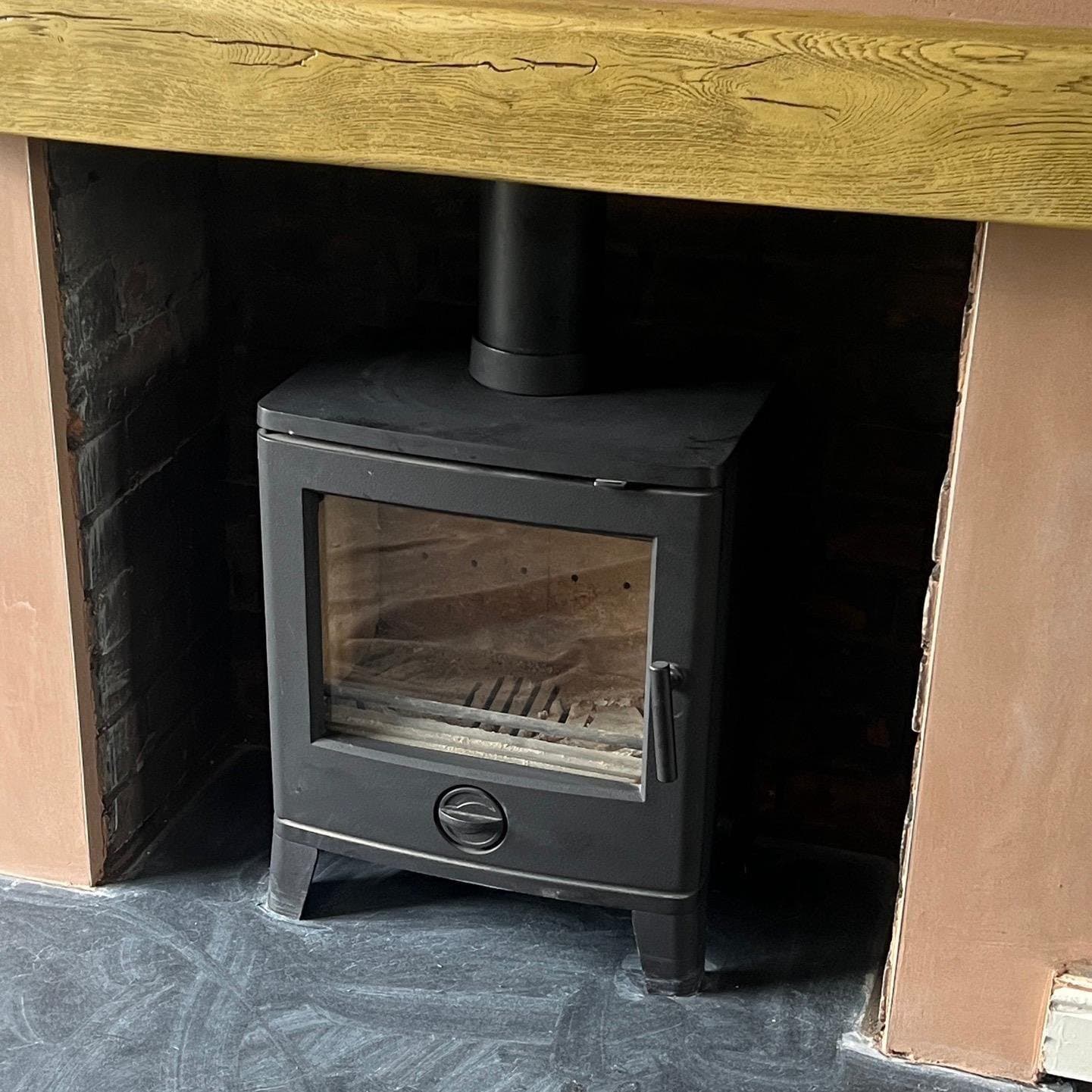 Compact stove installed beneath an oak beam in a rendered chamber