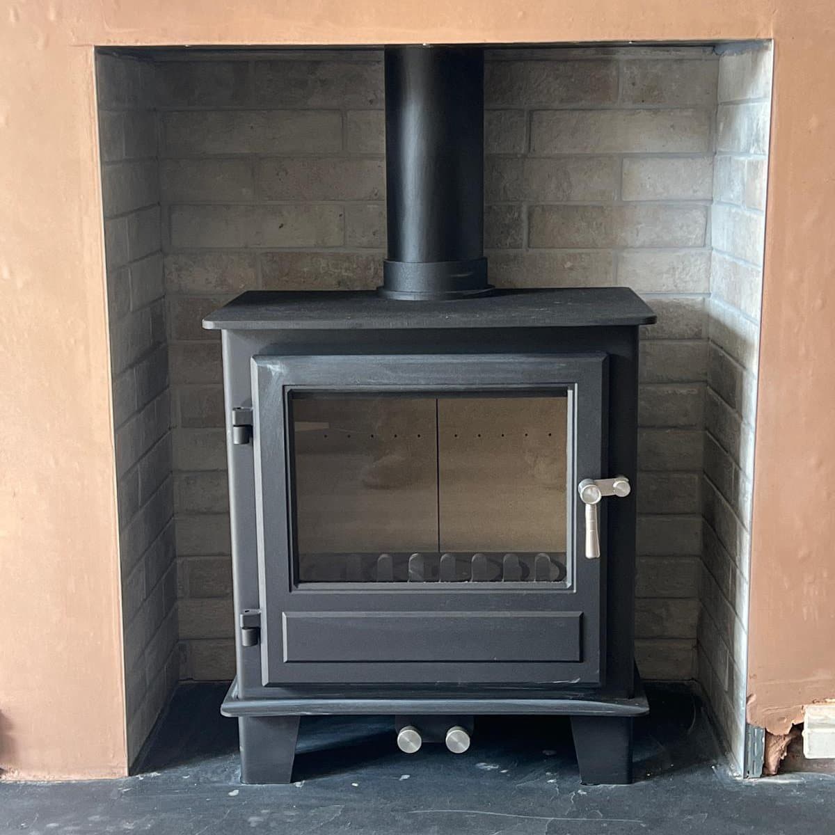 Multi fuel stove installed in a plain tiled chamber with a stone hearth