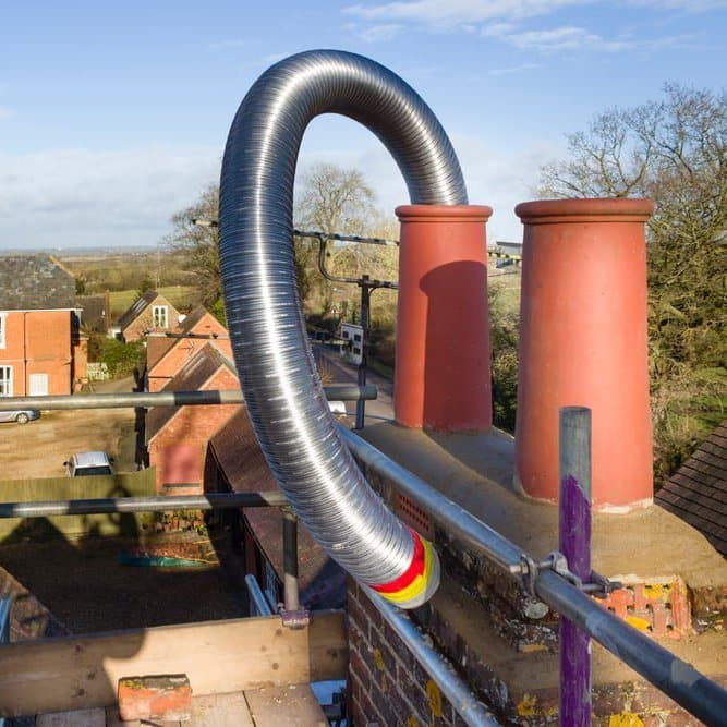 Flexible stainless steel chimney liner being fed down a chimney pot from the roof