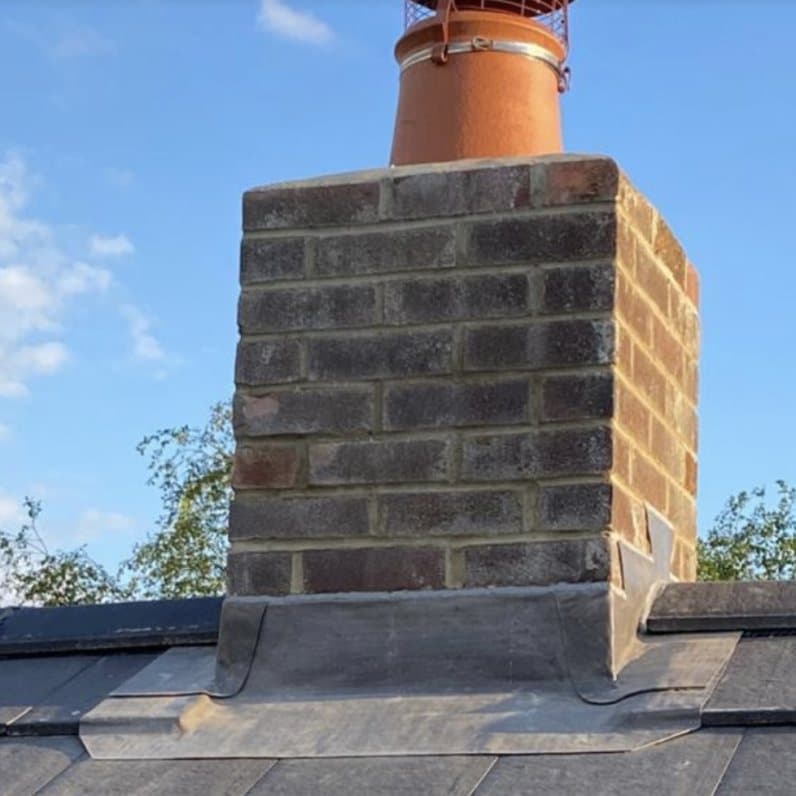 Rebuilt brick chimney stack with new terracotta pot on a slate roof