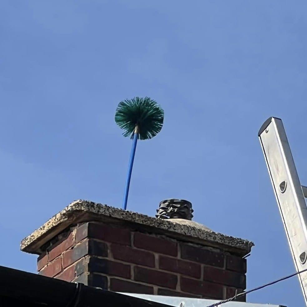 Chimney sweep brush head rising out of a chimney pot with a ladder against the stack